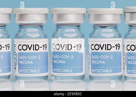 Fiale di vetro con vaccino COVID 19 poste sul tavolo in fila su sfondo blu Foto Stock
