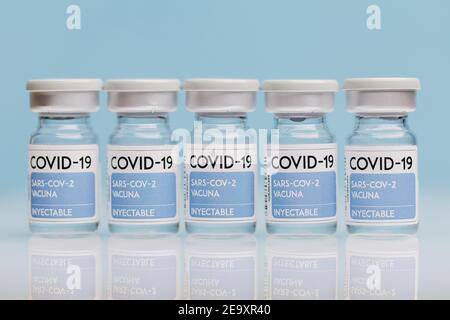 Fiale di vetro con vaccino COVID 19 poste sul tavolo in fila su sfondo blu Foto Stock