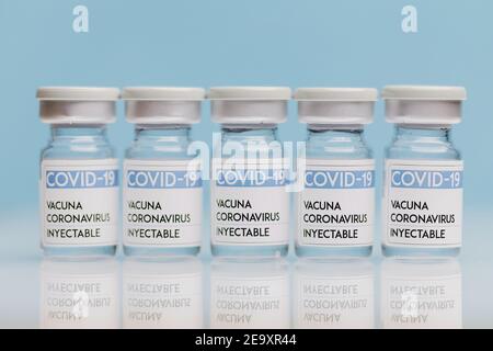 Fiale di vetro con vaccino COVID 19 poste sul tavolo in fila su sfondo blu Foto Stock