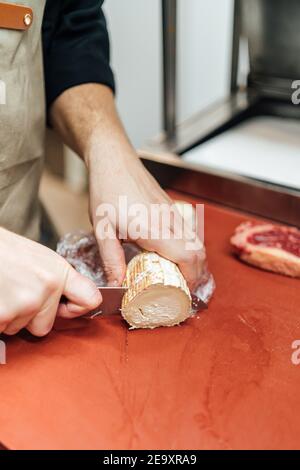 Crop faceless colpo di persona tagliando formaggio di capra in un cucina ristorante Foto Stock