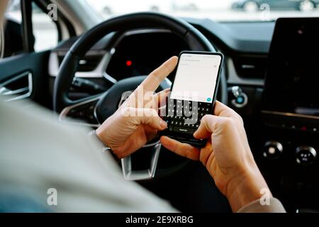 Coltivare imprenditore maschile irriconoscibile seduto sul sedile di guida nel lusso automobile e telefono mobile di navigazione Foto Stock