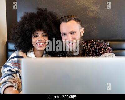 Contenuto multietnico Coppia di freelance seduti a tavolo con laptop e lavorando insieme sul progetto in cafe Foto Stock