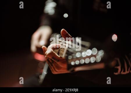 Chitarrista con vista laterale che suona la chitarra elettrica mentre si esibisce al buio monolocale con luce rossa Foto Stock