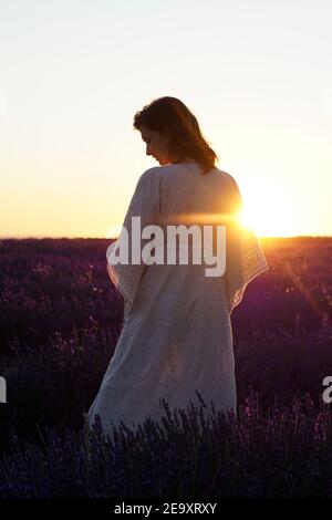 Vista posteriore di una donna tenera irriconoscibile in piedi maxi dress con in fiorente campo di lavanda sullo sfondo del cielo del tramonto Foto Stock