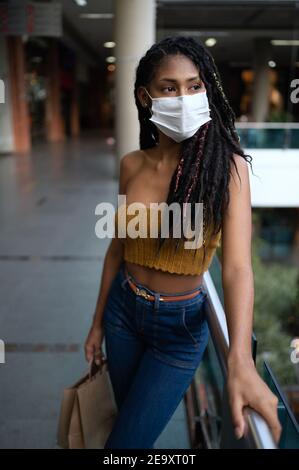 Ritratto di attraente giovane afro latin Woman con un facemask e tenendo borse per la spesa in centro commerciale, Colombia Foto Stock