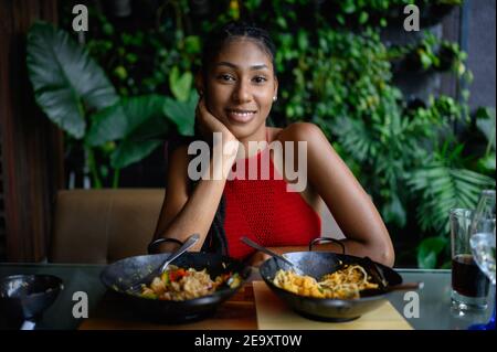 Ritratto di bella giovane afrolatina con dreadlock in una cima rossa uncinetto in posa in ristorante asiatico, Colombia Foto Stock