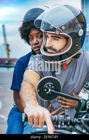 Giovane ragazzo etnico di stile e donna afroamericana in casual abiti e caschi seduti in moto sulla strada della città Foto Stock
