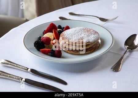 Da sopra piatto di gustosi frittelle con zucchero in polvere servito con frutti di bosco sani assortiti e fette di banana durante la colazione in caffè Foto Stock