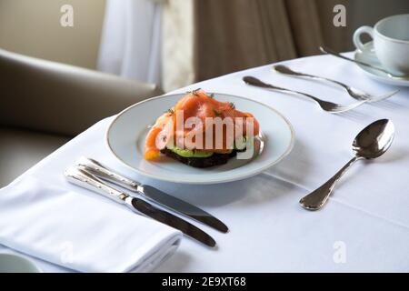 Piatto ad alto angolo con delizioso toast all'avocado con brindisi in camicia uova e salmone affumicato serviti a tavola con posate e. tazza di caffè durante la colazione in ho Foto Stock