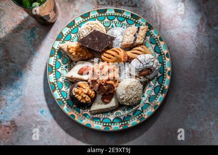 Dall'alto di baklava e biscotti con tè alla menta marocchina vicino coltello e forchetta posto sul tavolo decorato con menta foglie Foto Stock