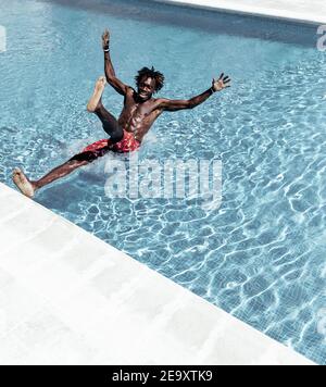 Uomo afroamericano stupito in pantaloncini che cadono in piscina Foto Stock