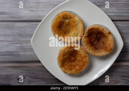 Tre budini tradizionali di bakewell seduti su un piatto bianco visto dall'alto verso il basso Foto Stock