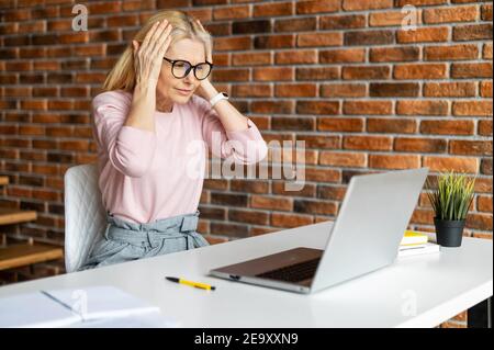 Donna d'affari di mezza età addetta a un look elegante e casual elegante che si starrà sullo schermo di un computer portatile in perdita, un dipendente femminile ha fatto un Foto Stock