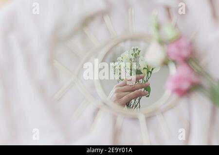 Mano che tiene fiori di manuka riflessa nello specchio su sfondo di tessuto morbido. Estetica primaverile. Buon giorno delle donne e delle madri. Concetto di salute mentale. Foto Stock