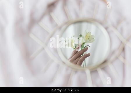 Mano che tiene fiori di alstroemeria riflessa in specchio su sfondo di tessuto morbido. Estetica primaverile. Buon giorno delle donne e delle madri. Salute mentale con Foto Stock