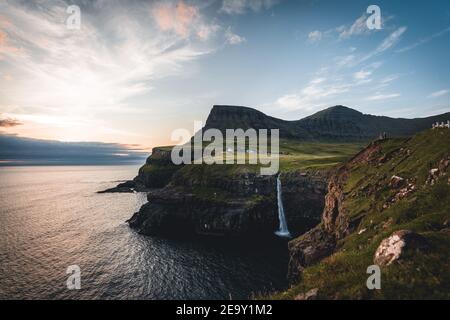 Gasadalur villaggio e Mulafossur la sua cascata iconica durante l'estate con il cielo blu. Vagar, Isole Faroe, Danimarca. Scorgo nel nord atlantico Foto Stock