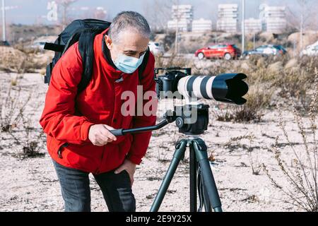 Fotografo che indossa una maschera chirurgica per scattare foto e video sul strada utilizzando un treppiede Foto Stock