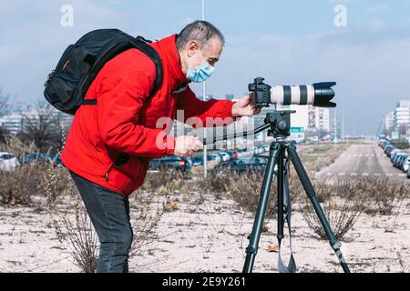 Fotografo che indossa una maschera chirurgica per scattare foto e video sul strada utilizzando un treppiede Foto Stock