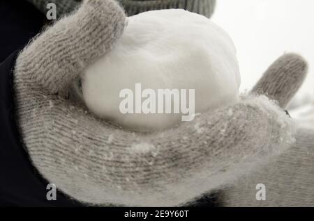 Una palla di neve fatta di neve appena arata, in una mano in un guanto di lana grigio. Foto Stock