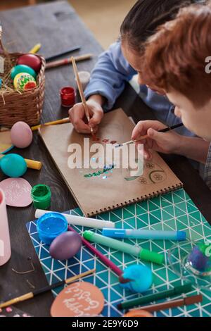 Primo piano di bambini che disegnano uova di Pasqua su carta seduta a. il tavolo Foto Stock