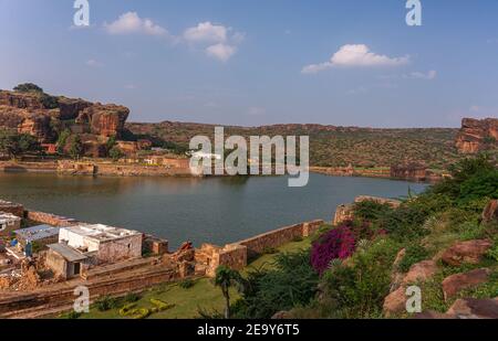 Badami, Karnataka, India - 7 novembre 2013: Templi in grotta sopra il lago Agasthya come mostrato, circondati da colline, rocce e scogliere sotto il paesaggio blu nuvoloso. Foto Stock