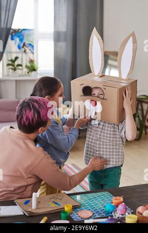 Madre che mette il costume di coniglio dalla scatola di cartone su suo figlio Preparandosi per la festa di Pasqua Foto Stock