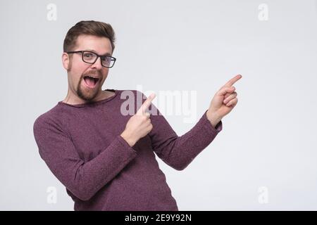 Uomo caucasico in occhiali con due dita che puntano da parte. Scatto in studio Foto Stock