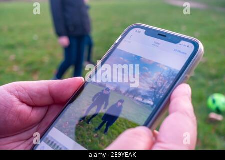 Una donna, con solo le mani visibili, rivede una fotografia dei suoi bambini scattata sul suo iPhone nel parco locale. Foto Stock