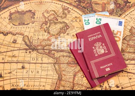 Passaporto spagnolo con bollette in euro all'interno, su una mappa del mondo per i viaggiatori. Foto Stock