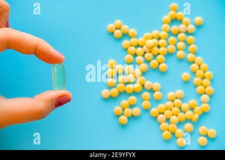 la mano femminile tiene la capsula di omega, molte piccole pillole gialle spruzzate su sfondo blu Foto Stock