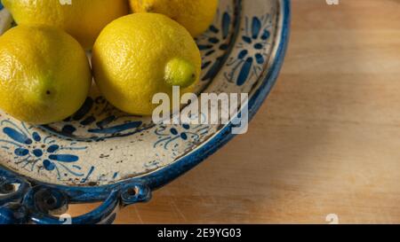 Limoni mediterranei freschi su una bella lastra di ceramica antica dipinta blu e beige su un tavolo di legno. Primo piano. Foto Stock