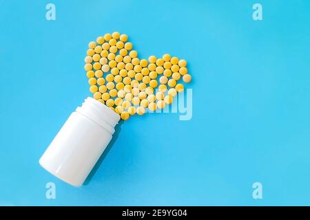 molte piccole pillole gialle versate da un vaso bianco su sfondo blu a forma di cuore Foto Stock