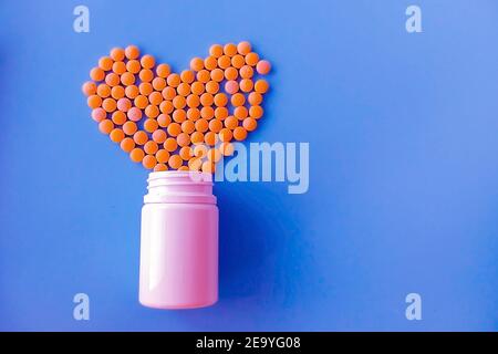 molte piccole pillole gialle versate da un vaso bianco su sfondo blu a forma di cuore Foto Stock