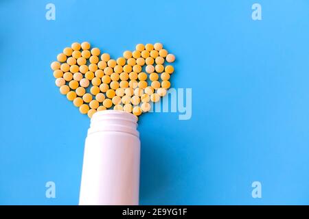 molte piccole pillole gialle versate da un vaso bianco su sfondo blu a forma di cuore Foto Stock