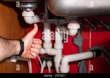 Controllare il circuito di drenaggio dell'acqua sotto il lavello della cucina. Problemi idraulici, lavori relativi al rubinetto che perde. Le mani dell'uomo controllano il serraggio del pi Foto Stock