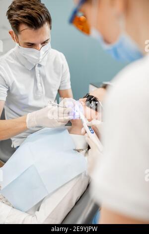 Dentista maschile e assistente utilizzando luce di cura dentale Foto Stock