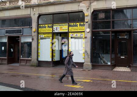 Una persona cammina attraverso negozi chiusi su Queen Street a Cardiff, Galles. Foto Stock