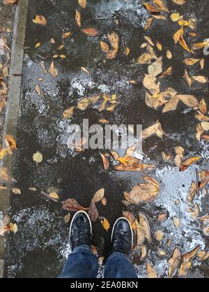 un piede maschio in sneakers in un puddle con autunno foglie Foto Stock