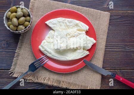 Cucina balcanica. Montenegro. Formaggio Pljevaljski - formaggio locale bianco morbido in piatto rosso su un tavolo rustico scuro. Spazio di copia Foto Stock