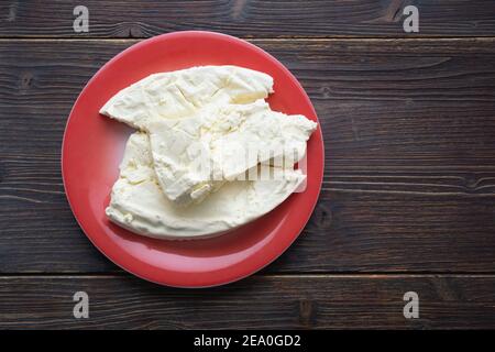 Cucina balcanica. Montenegro. Formaggio Pljevaljski - formaggio locale bianco morbido in piatto rosso su un tavolo rustico scuro. Spazio di copia Foto Stock