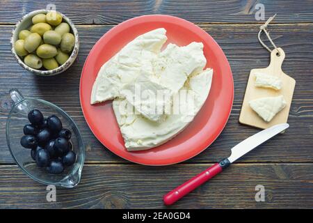 Cucina balcanica. Montenegro. Formaggio Pljevaljski - formaggio locale bianco morbido in piatto rosso su un tavolo rustico scuro Foto Stock