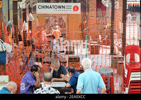 Chinatown, Singapore 3 Feb 21: Uomini di mezza età che giocano a Scacchi cinesi, mentre altri guardano a distanza di sicurezza dietro scherma di plastica Foto Stock