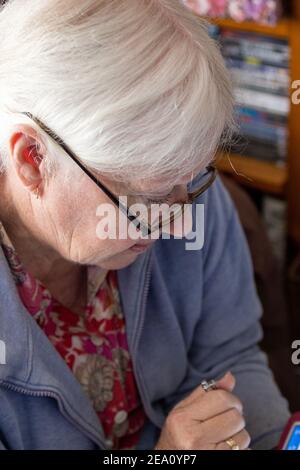 Una donna anziana con gli occhiali guardando giù leggere con la penna in mano con la messa a fuoco selettiva sull'occhio Foto Stock