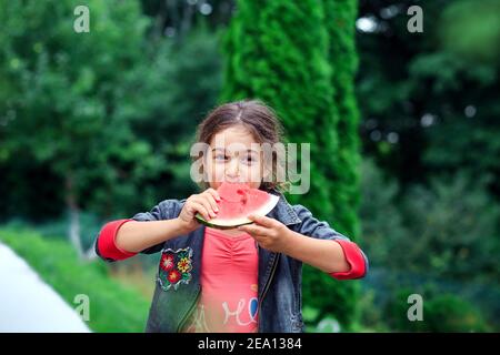 Piccola bella ragazza che mangia un succoso anguria in giardino. I bambini mangiano frutta all'aperto. Cibo sano per i bambini. Foto Stock