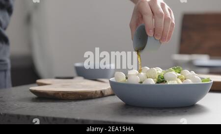 uomo versare condimento su insalata con kale, mozzarella, avocado e pomodori ciliegini, foto ampia Foto Stock