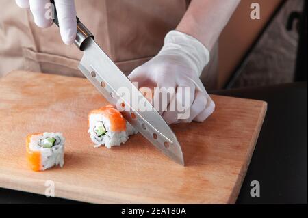 L'uomo cuoce il sushi su tavola di legno in guanti per una cottura sicura. Foto Stock
