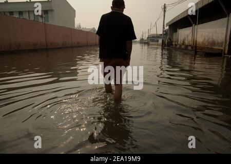 Un uomo che cammina lungo una strada allagata da acqua di mare a Penjaringan, nella zona costiera di Giacarta, Indonesia. Foto Stock