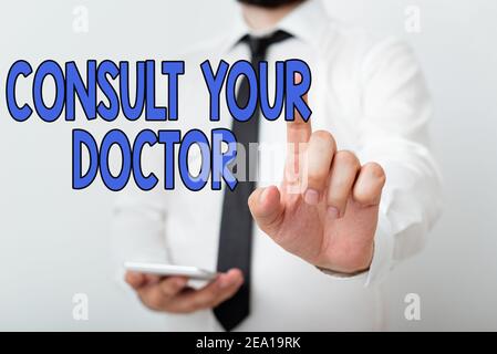 Cartello con scritto Consult Your Doctor. Foto di business showcase chiedere informazioni o consigli da un medico professionista modello con la mano punta dito Foto Stock