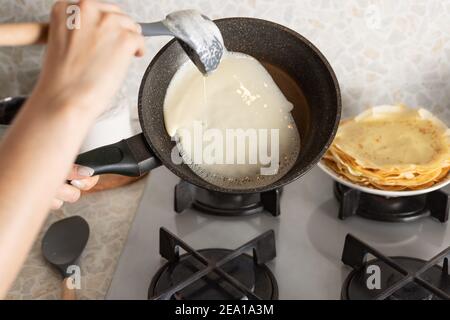 le mani femminili cucinano frittelle sottili sulla padella. Pancake fatti in casa Foto Stock