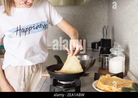 donna sorridente che cucinava frittelle sottili, crepes in cucina Foto Stock